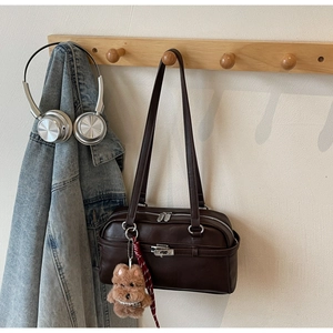 Detail view of dark brown leather shoulder bag with plush bear charm and silver hardware