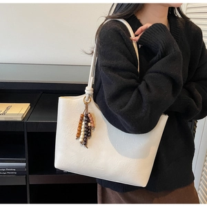 Detail view of white pleated tote bag with ethnic style wooden beaded fringe tassel