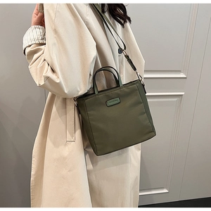 Olive green nylon tote bag with adjustable shoulder strap worn with a beige trench coat