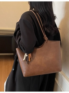 Brown high-capacity minimalist tote bag with decorative tassel charm shown on shoulder