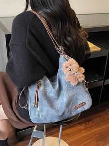 Vintage blue canvas hobo bag with brown leather strap and plush bear charm on a model