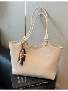 Minimalist off-white leather tote bag with long straps and colorful beaded charm