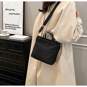 Detail of black nylon crossbody tote bag worn with a stylish beige trench coat