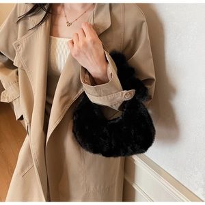 Dettaglio di una borsa in pelliccia sintetica nera soffice portata con un trench elegante