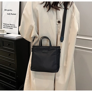 Detail of black fabric crossbody bag with wide strap worn over a beige trench coat