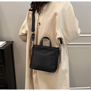 Detailed side view of black waterproof nylon crossbody bag styled with a beige coat
