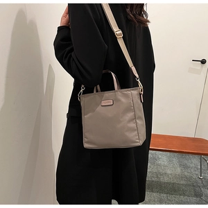 Detail of grey nylon tote bag with leather logo patch and adjustable shoulder strap