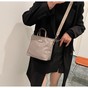 Detail of grey nylon crossbody bucket bag with wide strap and metal logo on model