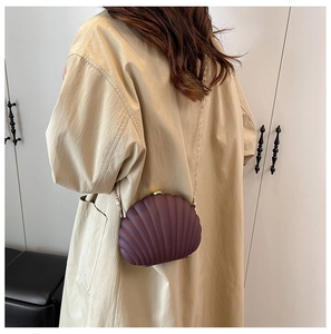 Détail du sac coquillage bordeaux avec chaîne dorée sur un trench-coat beige