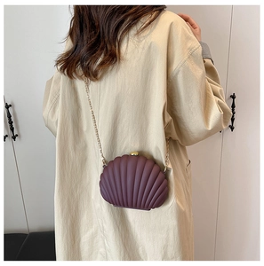 Sac bandoulière en forme de coquillage violet foncé porté par un mannequin avec chaîne