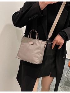 Beige nylon bucket bag with dual handles and wide strap worn with a black suit