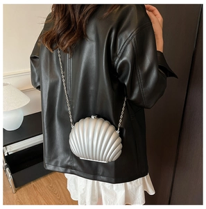 Sac coquillage argenté porté par un mannequin avec veste en cuir et jupe blanche