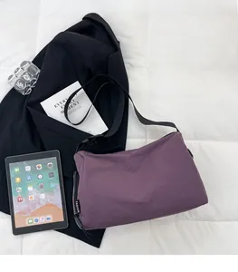Detail view of purple nylon crossbody bag with fashion label on a white quilted surface