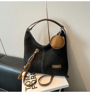 Close-up of black frosted tote bag with brown leather handles and small round coin purse