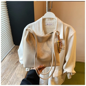 Detail of a minimalist cream tote bag with wooden bead charm and smooth leather finish