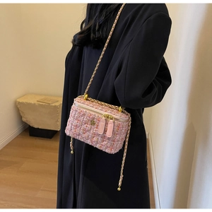 Détail d'un sac bandoulière en tweed rose avec fermoir floral en métal sur un manteau noir