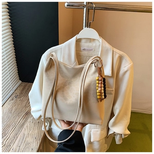 Detail of a beige faux leather bucket bag with ethnic beaded tassel on a white blazer