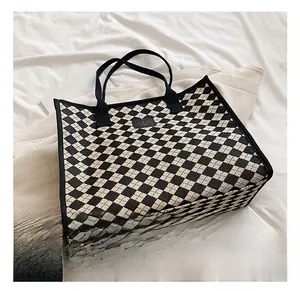 Detail of knit checkerboard tote bag with black woven handles and logo patch