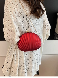 Sac bandoulière rouge en forme de coquillage avec chaîne dorée sur pull blanc