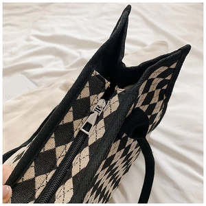 Detail view of checkerboard canvas tote with top zipper closure and black handles
