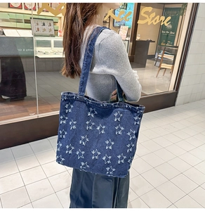 Detail of blue denim tote bag with white frayed star patches worn on the shoulder