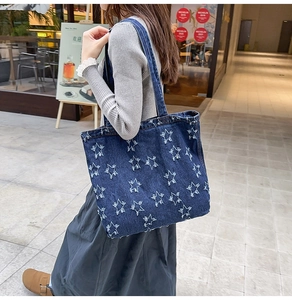 Deep blue denim tote bag with white frayed star patterns shown in a street style view