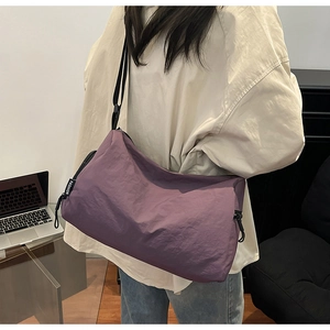 Detail view of large purple crossbody bag with fashion label and adjustable strap