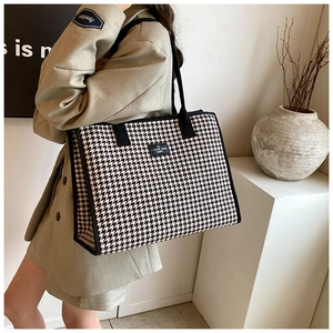 Detail of checkered canvas tote bag with black strap handle worn with beige blazer