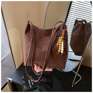 Detail of a brown suede shoulder bag featuring a unique wooden bead tassel and gold ring