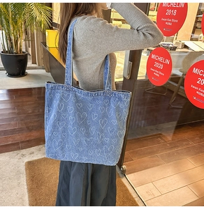 Close-up of blue washed denim tote bag with white heart pattern carried by a model