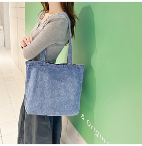 Blue denim tote bag with white heart prints shown on model for size and drape