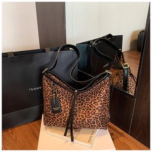 Close-up of leopard print tote bag featuring black leather straps and gold metal buckles