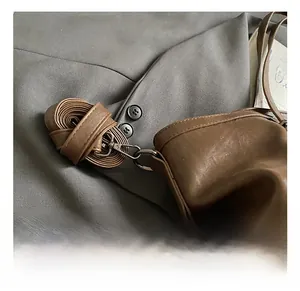 Détail d'un sac en cuir marron avec crochet gris anthracite et bandoulière tissée