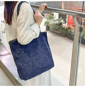 Detailed close-up of dark blue denim tote bag with white hand-drawn heart patterns
