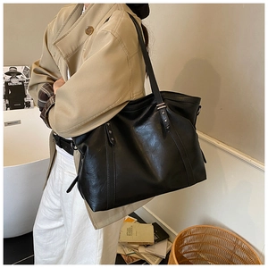 Gros plan d'un grand sac cabas noir en similicuir avec rivets étoilés sur un trench beige