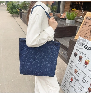 Deep blue denim tote bag with light blue heart pattern worn by model in a cafe