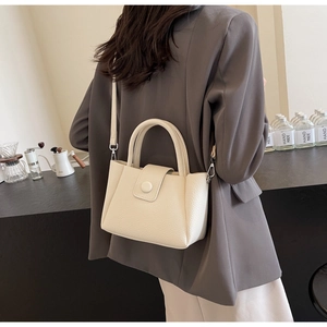 Détail du sac seau crème avec texture litchi et boucle décorative ronde élégante