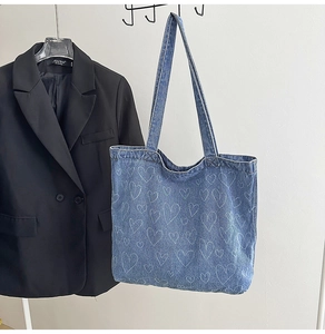 Hanging blue denim tote bag with white heart line art pattern next to a black blazer