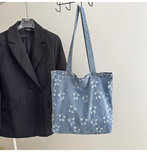 Detail of frayed edge star embroidery on washed denim canvas tote bag hanging with suit