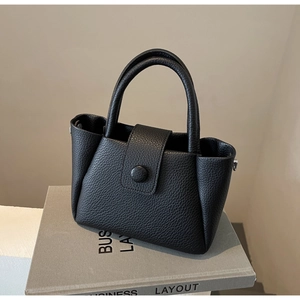 Détail du sac seau en cuir noir grainé avec doubles anses et boucle sur un support