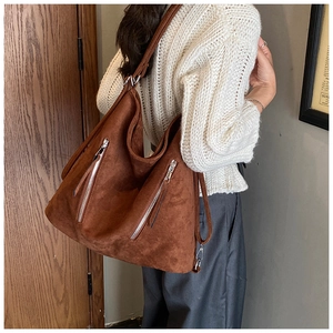 Détail du sac hobo en daim marron avec doubles fermetures éclair verticales et crochets métal