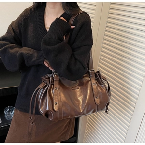Detail of a deep brown vintage tote bag featuring side drawstrings and a metal logo plaque