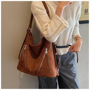 Détail d'un sac cabas en daim marron avec fermetures éclair argentées et bandoulière large