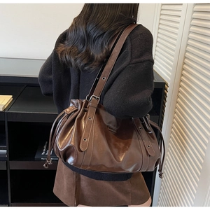 Detail of a dark brown glossy leather shoulder bag with drawstring pleats and metal eyelets
