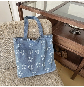 Close-up of denim tote bag with white star embroidery on a beige woven armchair
