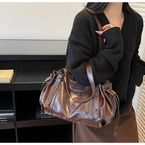 Detail of a large dark brown tote bag featuring drawstring pleats and metal eyelets