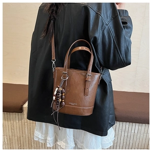 Detail einer braunen Eimer-Handtasche mit Vintage-Perlenanhänger und Tragegriffen