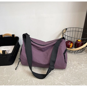 Close-up of a purple nylon crossbody bag with wide adjustable strap and Fashion label