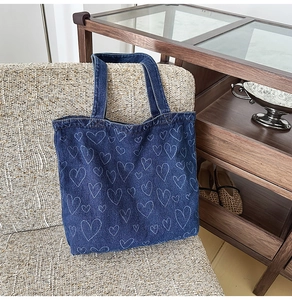 Close-up of washed denim tote bag featuring white hand-drawn heart patterns on a chair