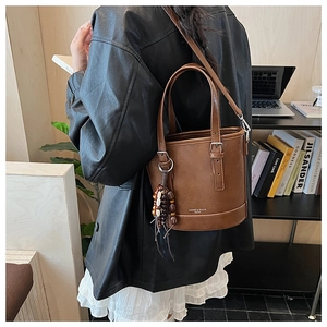 Nahaufnahme der braunen Leder-Eimertasche mit Holzperlen-Quasten und Logo-Gravur